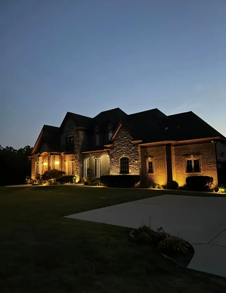 Warm landscape lights illuminating a brick and stone house at dusk