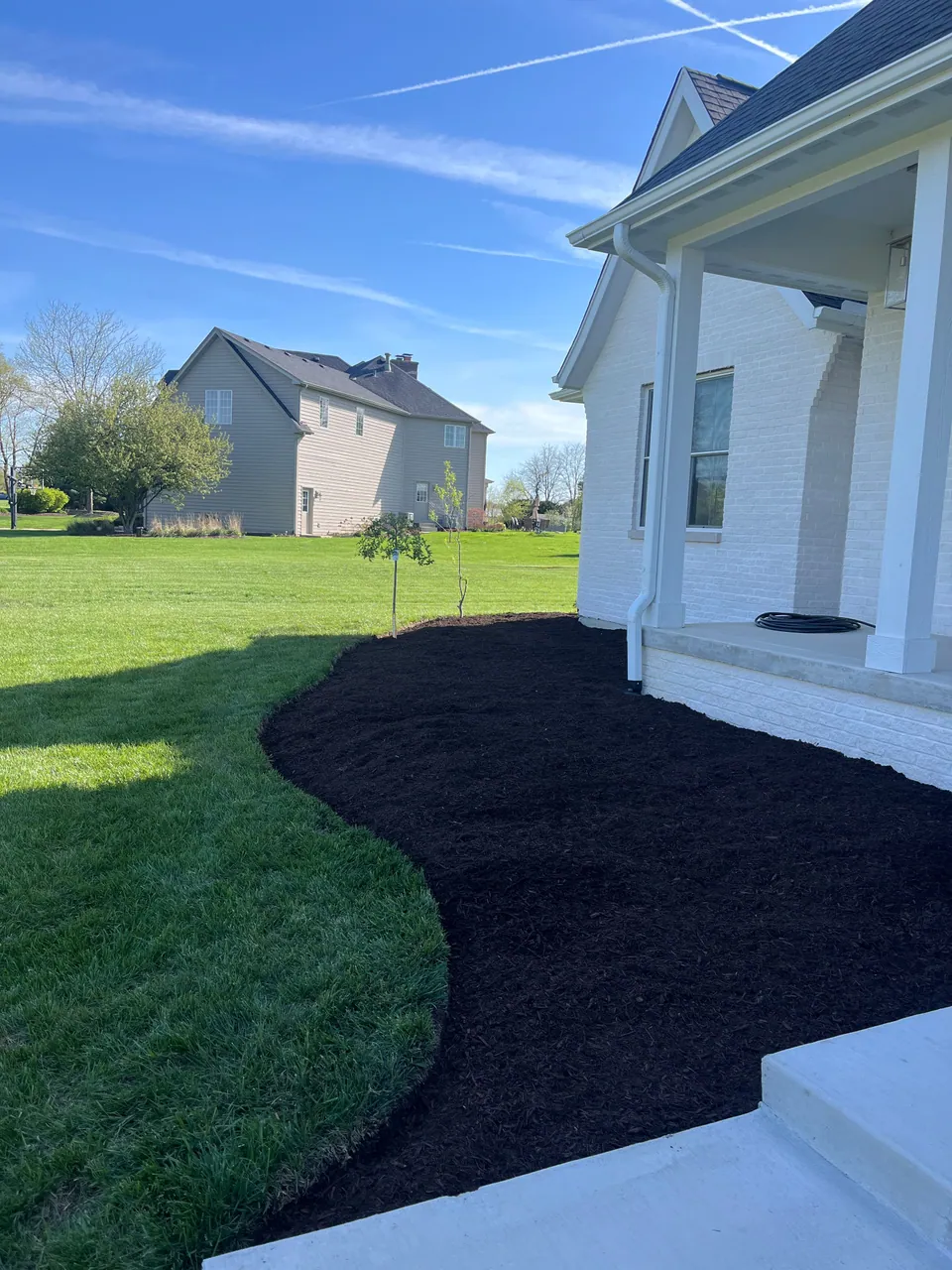 Dark mulch and a curved lawn edge beside a white brick porch